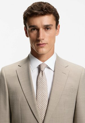 Completo color beige chiaro con tessuto strutturato, design monopetto, rever a lancia, abbinato a una cravatta a motivo chiaro e camicia bianca da uomo.