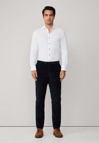 Witte overhemd met lange mouwen en beige knopen, gecombineerd met zwarte broek en bruine leren schoenen. Eenvoudig ontwerp, slim fit, gladde textuur.