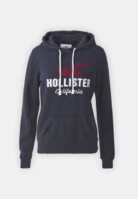 Mörkblå hoodie med framficka, vit text "HOLLISTER California" och röd fågallogo. Har dragsko i huvan och ribbade muddar.