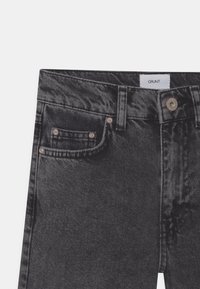 Sorte denimjeans med en let falmet tekstur. Funktioner inkluderer kobberfarvede nitter, et mærke ved taljen og fem-lomme design.