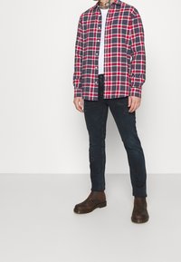 Camicia in flanella a quadri rossi e blu con chiusura a bottoni, abbinata a jeans skinny neri con dettagli consumati e stivali alla caviglia marroni.