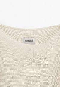 Pull en maille couleur crème avec col rond et une étiquette blanche portant l'inscription "MASSIMO DUTTI ÉDITION LIMITÉE" cousue à l'intérieur du col.