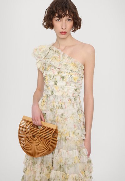 Floral ruffle jurk met één schouder in pastelkleuren, gecombineerd met een ronde geweven bamboetas met verticale latten en een handvat.