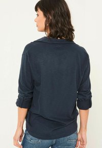 Marineblaue, leichte Bluse mit Kragen und hochgerollten Ärmeln. Weicher Stoff mit leichtem Glanz. Rückansicht zeigt minimale Details.
