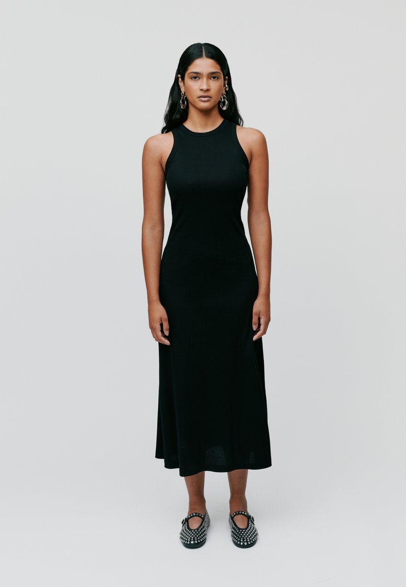 Black sleeveless midi dress with a fitted bodice and flared skirt; smooth texture. The model wears patterned black shoes with accents.