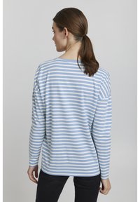 Csíkos, világoskék és fehér hosszú ujjú felső, laza szabással, kerek nyakkivágással és enyhén lejjebb helyezett vállakkal. Fekete nadrág nem tartozik hozzá.