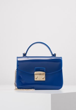 Glanzende blauwe handtas met een bovenhandvat, een sluiting in goudtint en een gouden kettingriem, tentoongesteld op een wit voetstuk tegen een neutrale achtergrond.