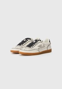 White leather sneakers with black laces, contrasting stitching, and a rubber gum sole. Features a stylized "Karl" logo on the side.