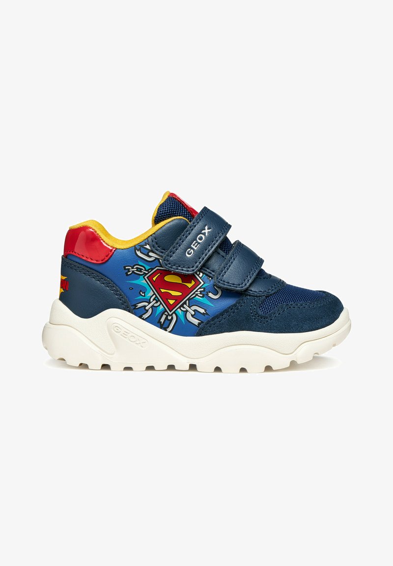 Baskets pour enfants bleu marine avec intérieur jaune, talon rouge, semelle blanche, deux bandes Velcro et logo Superman avec chaînes sur le côté.