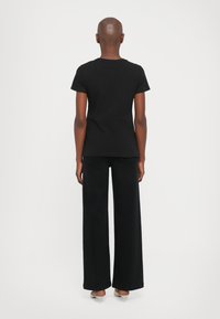 Zwarte katoenen T-shirt met korte mouwen, ronde hals, gecombineerd met zwarte wijde broek. De outfit heeft een gladde textuur en een minimalistisch ontwerp.