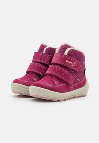 Ružové semišové topánky majú dva nastaviteľné Velcro remene, mäkké fleece podšívku a textúrovanú gumovú podrážku v svetlosivej farbe.