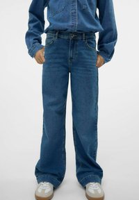 Bredbenta blå denimjeans med femfickdesign, ljus tvätt och knappstängning. Matchat med vita sneakers och en denimskjorta.