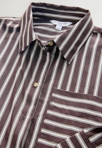 Braun gestreiftes kurzärmliges Hemd mit weißen und beigen Streifen, mit Button-Down-Kragen, Brusttasche und hellbraunen Knöpfen. Weicher Stoff. 