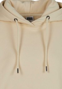 Felpa con cappuccio di colore crema, con coulisse, occhielli in tonalità argento e texture di tessuto morbido. Etichetta con la scritta "URBAN CLASSICS."