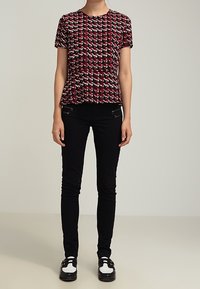 Czerwona i czarna bluzka z krótkim rękawem w wzór, z peplum, w połączeniu z wąskimi czarnymi spodniami i kontrastującymi czarno-białymi butami.