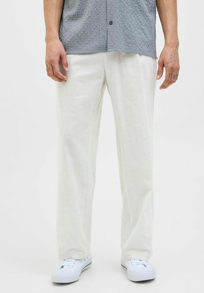 Pantalons clairs, amples, en tissu texturé, associés à des baskets blanches et à une chemise à manches courtes grise à motifs.