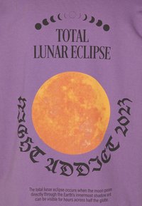 Camiseta gráfica púrpura con un gran diseño de luna naranja y texto negro que dice "ECLIPSE LUNAR TOTAL AGOSTO 2022" y detalles adicionales debajo.
