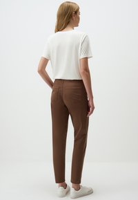 Pantaloni in cotone marroni con gambe affusolate, due tasche posteriori e una t-shirt bianca a maniche corte. L'outfit è completato da sneakers bianche.