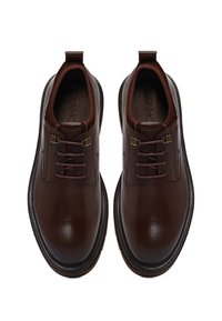 Een paar gepolijste donkerbruine leren veterschoenen met trekriempjes en dikke zwarte zolen, van bovenaf bekeken op een witte achtergrond.