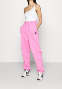 Pantaloni della tuta rosa realizzati in misto cotone con vita elastica, coulisse e tasche laterali. Presentano un piccolo logo sulla coscia.