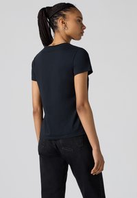 Black, short-sleeve t-shirt made of soft fabric, featuring a crew neck and fitted design, viewed from the back, worn with black jeans.