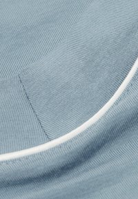 Jasnoniebieska tkanina o prążkowanej strukturze, z gładkim białym wykończeniem wzdłuż krawędzi. Powierzchnia jest lekko zakrzywiona.