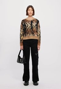 Fuzzy, brun och svartrandig tröja; svarta cargo-byxor; en stilren svart handväska; kraftiga svarta skor; modellen står mot en vit bakgrund.