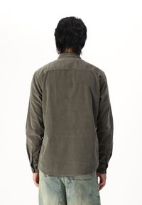 Chemise en velours côtelé vert olive avec des manches longues, des poignets à bouton et un col classique. Le tissu a une apparence douce et texturée.