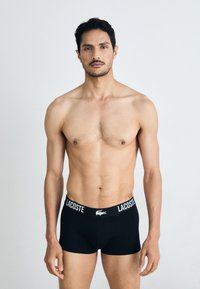 Black boxer shorts with a white waistband featuring the Lacoste logo. Soft, breathable fabric with a fitted design.