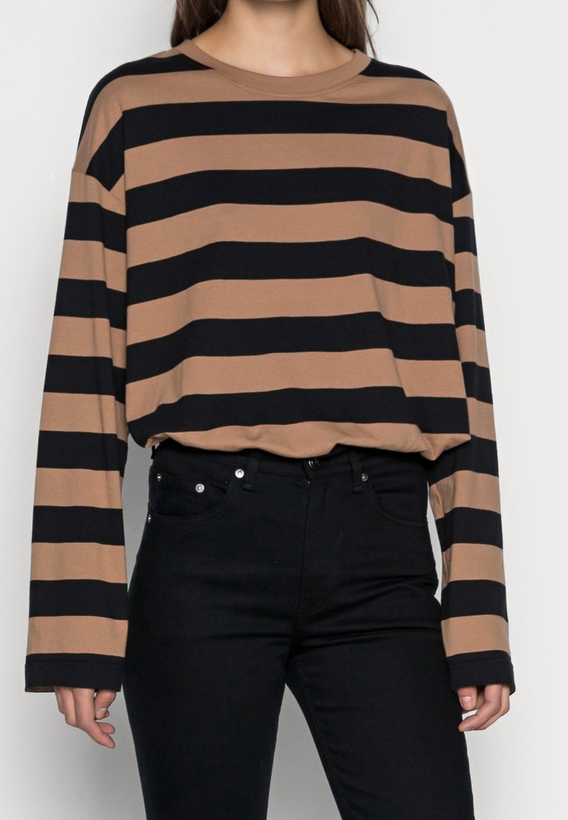 Brown and black striped long-sleeve shirt with a loose fit, crew neckline, and soft fabric, paired with black denim pants.