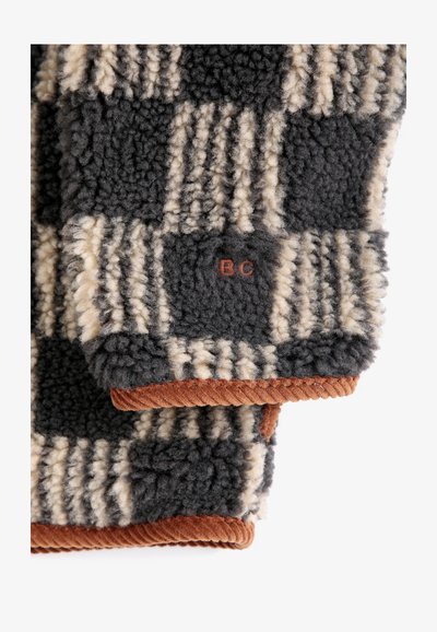 Gros plan d'un tissu polaire à carreaux noir et beige avec bordure en velours côtelé marron et lettres rouges brodées "BC."