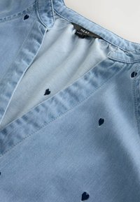 Jasnoniebieska dzianinowa bluzka z dekoltem w serek, granatową haftowaną serduszkową ozdobą i miękką fakturą. Wewnątrz przy dekolcie widoczna metka marki.