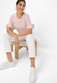  gestreepte T-shirt met korte mouwen in rood en wit, gecombineerd met opgerolde witte broek en witte sneakers, zittend op een houten stoel.