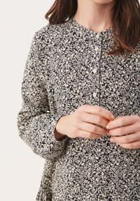 Mustakalla ja valkoisia kukkakuosisia nappimekkoja pitkähihaisilla hihoilla, pyöreällä kaula-aukolla ja väljällä istuvuudella, valmistettu kevyestä kankaasta.