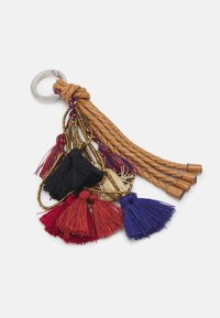 Spleciony brązowy skórzany brelok z wielokolorowymi frędzlami w kolorze czarnym, czerwonym, kremowym i niebieskim, oraz małymi złotymi łańcuszkami na srebrnym pierścieniu.