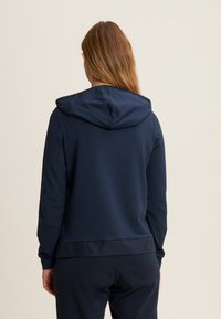 Felpa navy con cappuccio regolabile, maniche lunghe e orlo a costine. Texture liscia, design minimale e senza loghi o motivi visibili.