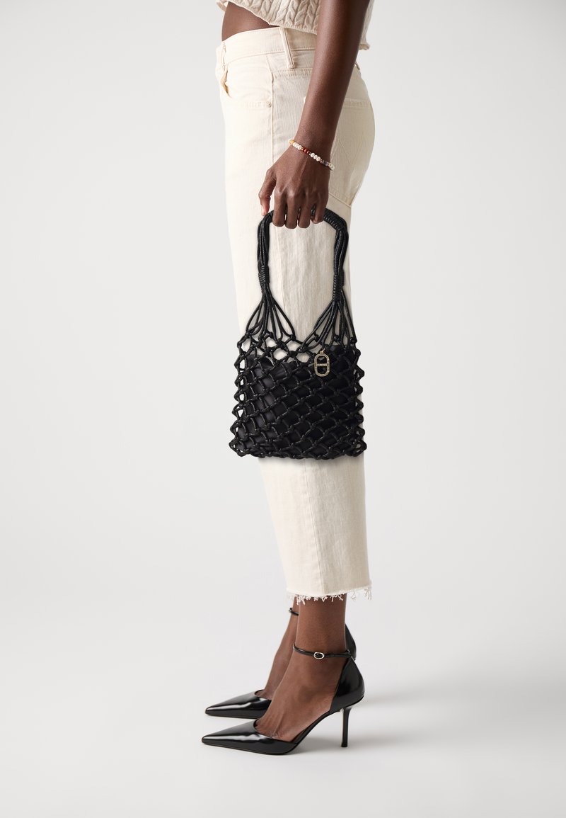 Sac à main tissé noir avec un design en filet texturé et un fermoir doré. Complété par un pantalon de couleur claire et des escarpins noirs à bout pointu.