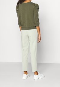 Olivgrön tröja med puffärmar, i kombination med ljusgrå avsmalnande byxor och vita sneakers. Slät textur, avslappnad design.