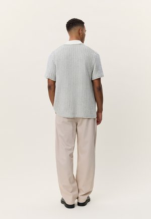 Πλεκτό πόλο μπλουζάκι με κοντά μανίκια σε ανοιχτό γκρι χρώμα με λευκό γιακά, σε συνδυασμό με φαρδιά μπεζ παντελόνια και μαύρα παπούτσια.