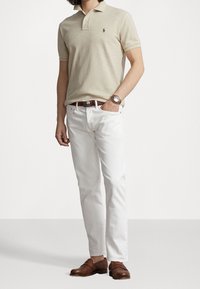 Beżowa koszulka polo z krótkim rękawem, białe dżinsy, brązowe skórzane buty i srebrny zegarek. Klasyczny design z minimalistycznymi detalami.