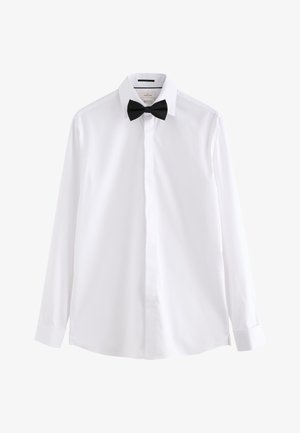 Camicia bianca a maniche lunghe con bottoni nascosti e papillon nero preannodato su sfondo bianco.