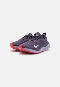 Scarpe sportive viola con tomaia texturizzata, intersuola di un viola chiaro e suola in gomma rosa. Presentano un logo bianco e dettagli verdi.