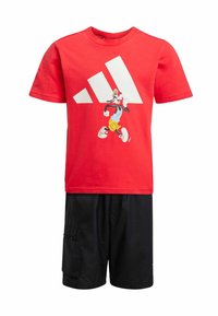 Červené bavlněné tričko s grafikou Goofy a bílým logem Adidas, v kombinaci s černými šortkami se zipem a hladkou texturou.