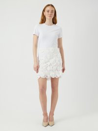 T-shirt blanc à manches courtes associé à une mini-jupe blanche en dentelle avec des motifs floraux et un ourlet festonné, complété par des talons beiges.