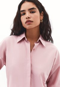 Lyserød button-up skjorte med krave, afslappet pasform og korte ærmer. Har en frontplacket med en enkelt knapdetalje.