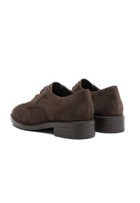 Scarpe eleganti da uomo in suede marrone scuro, con tacco basso impilato e dettagli brogue, viste da un'angolazione tre quarti posteriore.