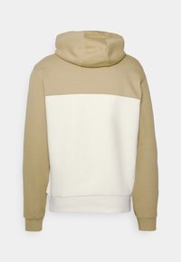 Sudadera con capucha que presenta una parte superior beige y una parte inferior crema. Está hecha de una tela suave con puños y dobladillo de canalé.