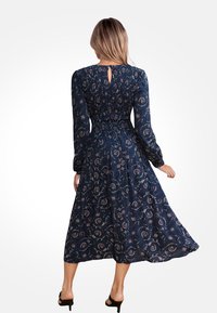 Granatowa sukienka w kwiatowy wzór, z długimi rękawami, zdobieniem w pasie i wycięciem na plecach. Gładki materiał z długością midi.