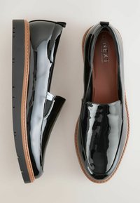 Melnas lakotas ādas slip-on kurpes ar zemu profilu, noapaļotu purngalu un brūniem gumijas zole. Iekļautas elastīgas sānu paneļi ērtai uzvilkšanai.