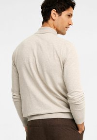 Beiger Strickpullover mit Kragen, langen Ärmeln und lockerer Passform. Der Stoff hat eine glatte Textur und einen gerippten Saum.